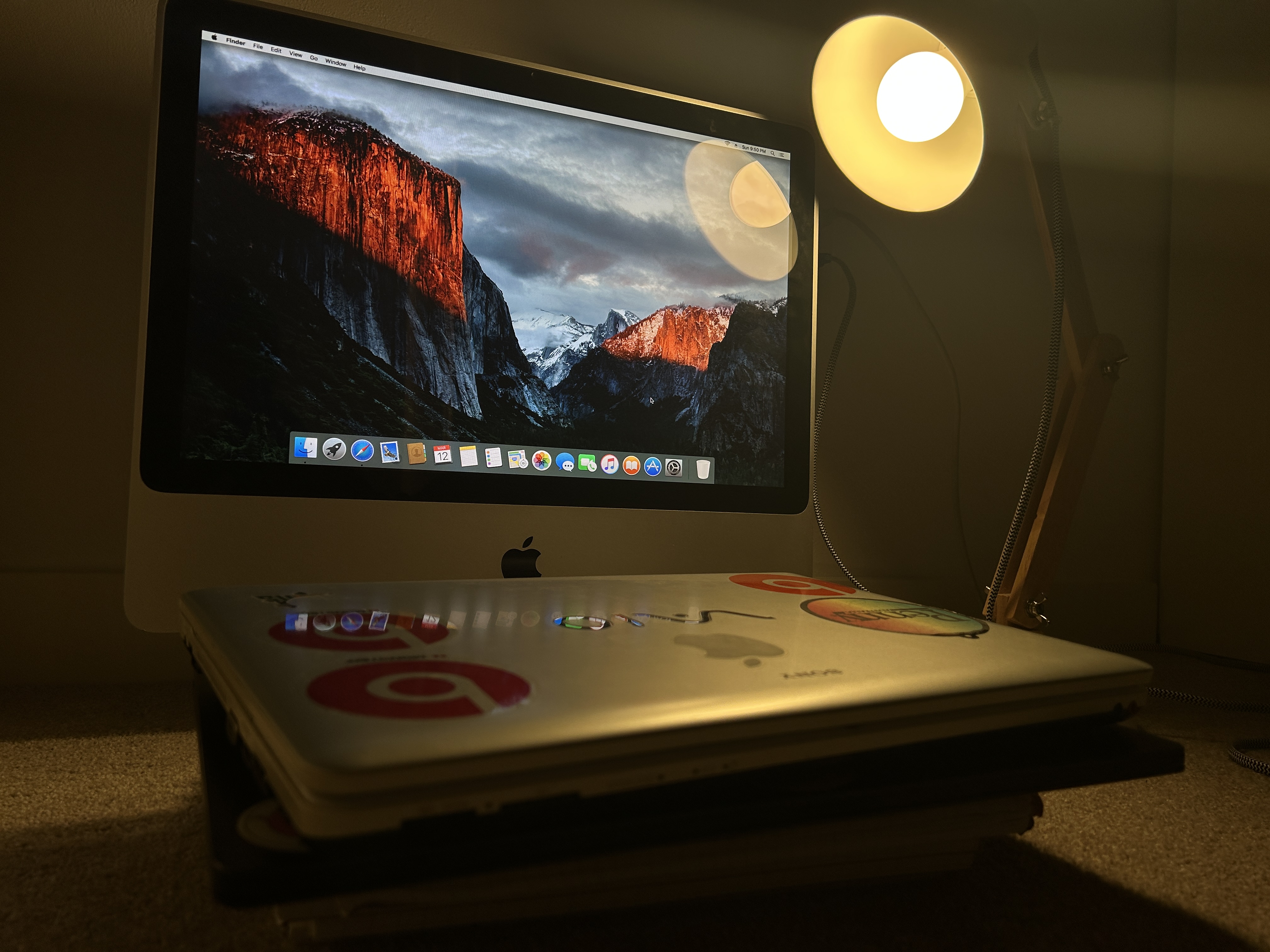 An old iMac and a pile of old laptops in a warm light
